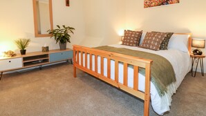 A bedroom with a wooden bed, a bedside table, a nightstand, a mirror, a potted plant, and a painting on the wall. - 8 Church Lane (Stoke-on-Trent)