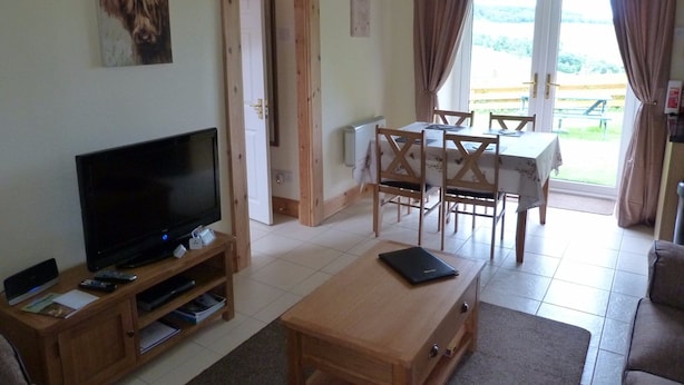 Ein Wohnzimmer mit Fernseher, Holzmöbeln und einem Essbereich mit Tisch und Stühlen.