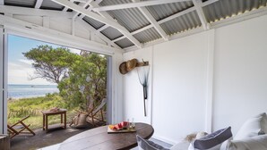 Une pièce avec vue sur la mer, une table ronde en bois sur laquelle est disposé un plateau de fruits, et un canapé agrémenté de coussins.