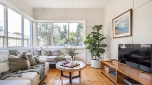 Un salon comprenant un canapé, une table basse avec un jeu d’échecs, une grande plante, un téléviseur et des étagères à livres.