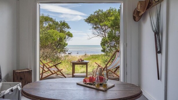 Une vue sur la plage depuis une chambre avec une table ronde, un hamac et une table en bois sur laquelle se trouvent une pastèque et des boissons.