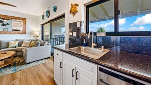 A modern kitchen with a large window, white cabinets, and a stainless steel dishwasher.