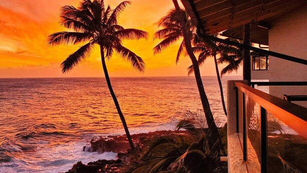 A sunset view with palm trees and a beach.
