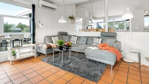 A modern living room with a grey sofa, a coffee table, and a rug. There is a window with a view of the outside, and an air conditioning unit on the wall. - "Josef" - 950m from the sea by Interhome (Fanø)