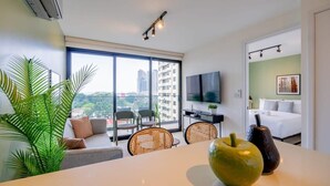 A modern hotel room with a large window, a flat-screen TV, a dining area with a table and chairs, and a bed with a white duvet. - w* | Polished 1BR in San Francisco w/ Balcony View (Panamá)
