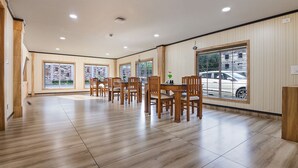 A spacious dining area with wooden tables and chairs, large windows with views of the outside, and a tiled floor. - SANJEEVINI AYURVEDA AND YOGA RETREAT (Aluva)