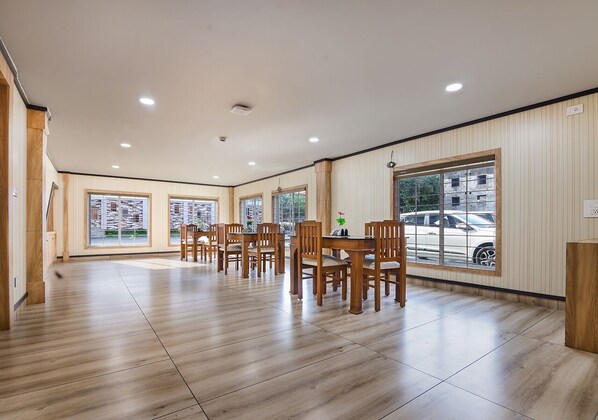 Un'ampia sala da pranzo con tavoli e sedie in legno, grandi finestre con vista sull'esterno e pavimento piastrellato.