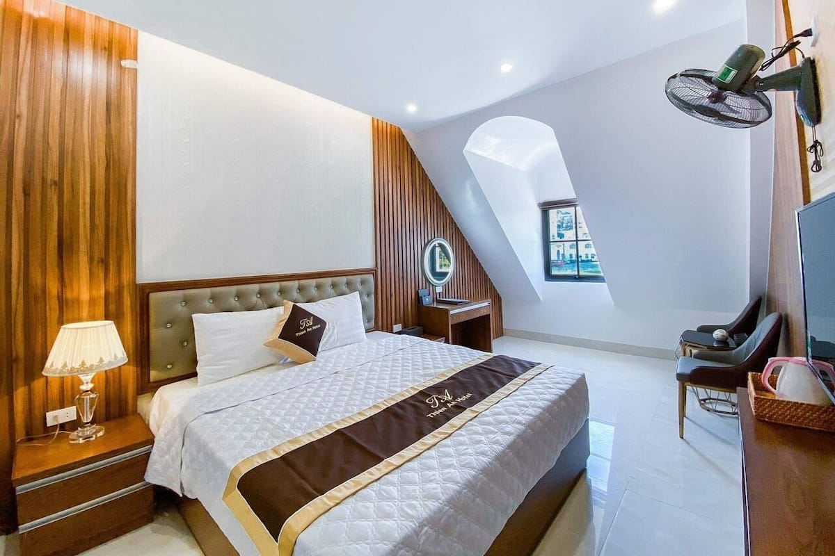 A modern hotel room with a large bed, a desk, a chair, a TV, and a window with a view.