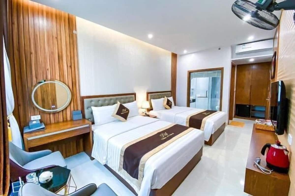 A hotel room with two beds, a desk, a chair, a mirror, a TV, and a kettle.
