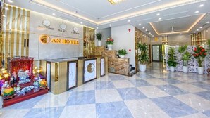 A hotel reception area with a check-in counter, decorative plants, and a marble floor. - An Hotel Ha Long (Bai Chay)