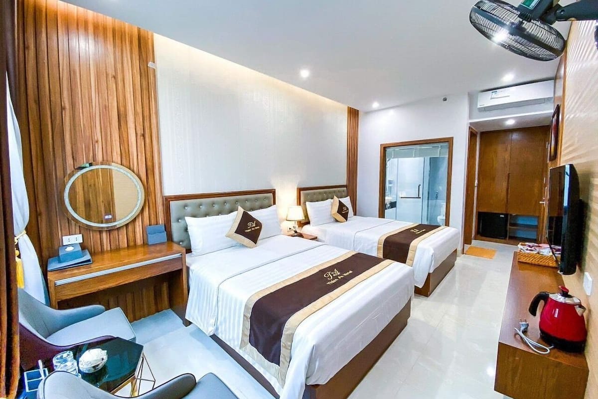 A hotel room with two beds, a desk, a chair, a mirror, and a TV.