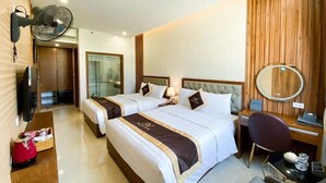 A hotel room with two beds, a desk, a chair, a TV, a fan, and a wooden wall panel. - An Hotel Ha Long (Bai Chay)