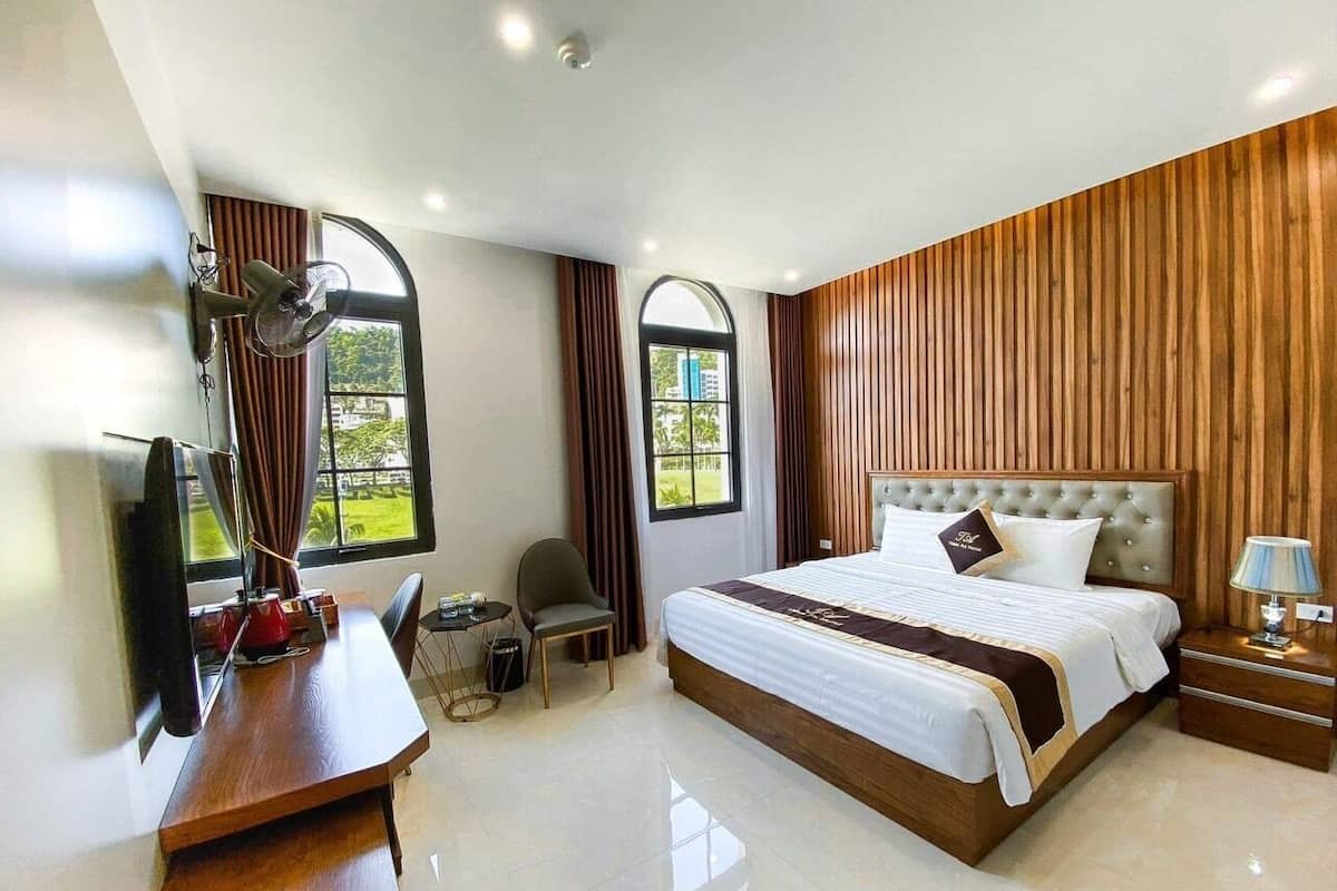 A hotel room with a large bed, a desk with a chair, a TV, and a window with curtains.