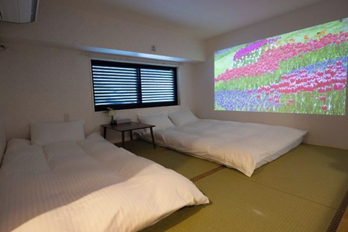 A hotel room with two beds, a small table, and a projection screen displaying a colorful image.