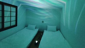 A room with two beds, a window, and a wall displaying a light projection of the aurora borealis. - Hotel Belle Via Tokyo (Tokyo)