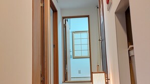 A hallway with a wooden door on the left, a window at the end, and a red fire alarm on the right. - Hotel Belle Via Tokyo (Tokyo)