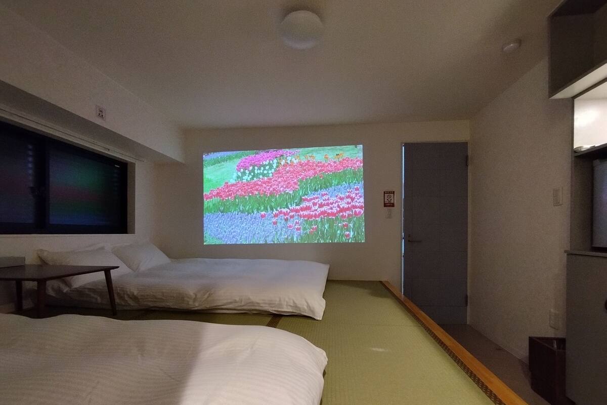 A hotel room with two beds, a large window, and a projection screen displaying a colorful image.