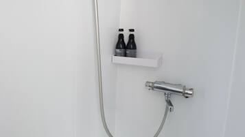 A shower with a handheld showerhead and a wall-mounted faucet. There is a shelf with two bottles of shampoo and conditioner.