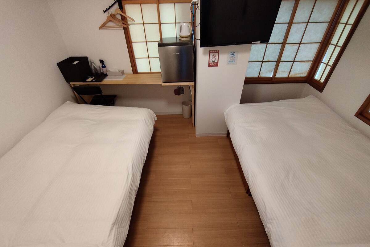 A compact room with two single beds, a small desk with a computer, and a TV mounted on the wall.
