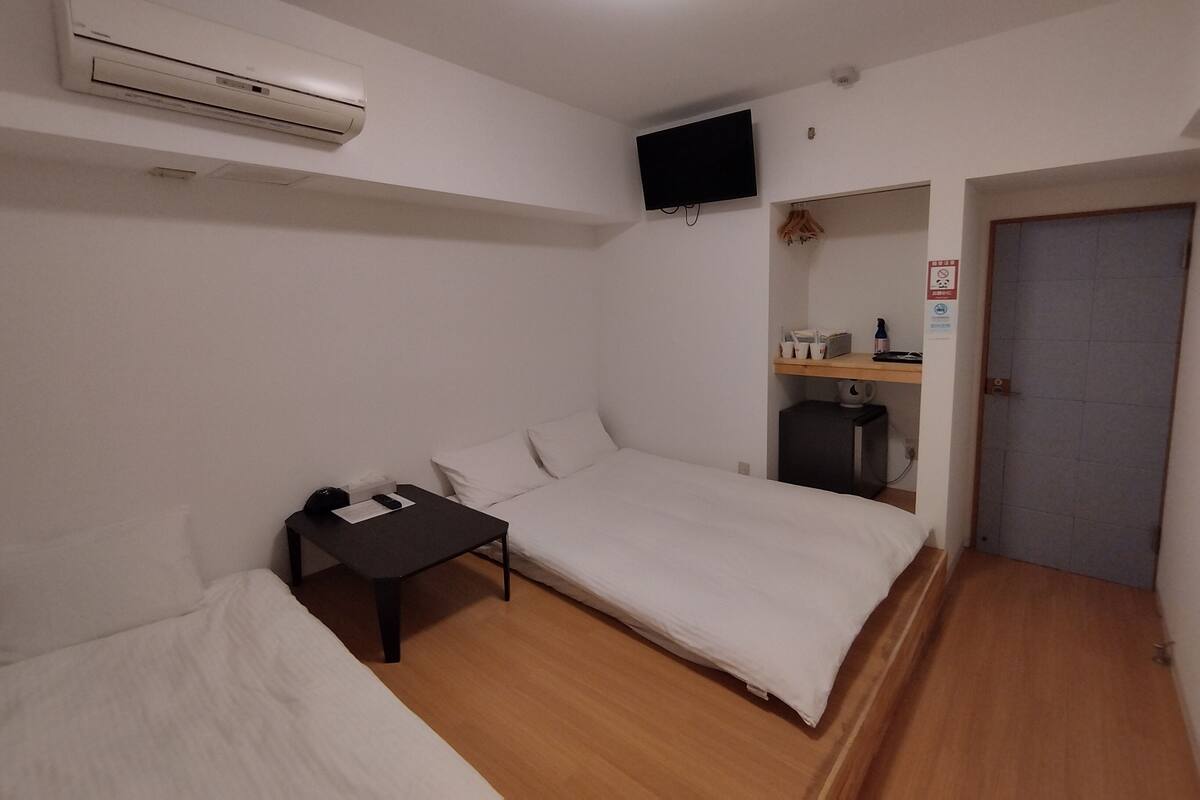 A small, clean room with a bed, a desk, a chair, a TV, and a door.