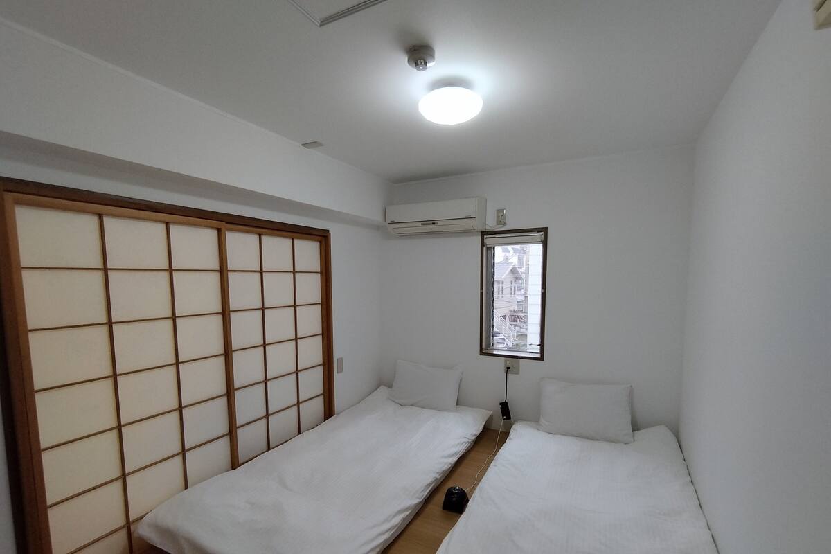 A room with two beds, a sliding shoji screen, a window with a view, and an air conditioning unit.