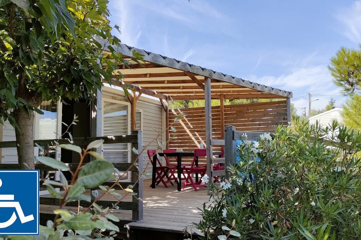 A covered outdoor area with a wooden deck, a table with chairs, and a wheelchair accessibility sign.