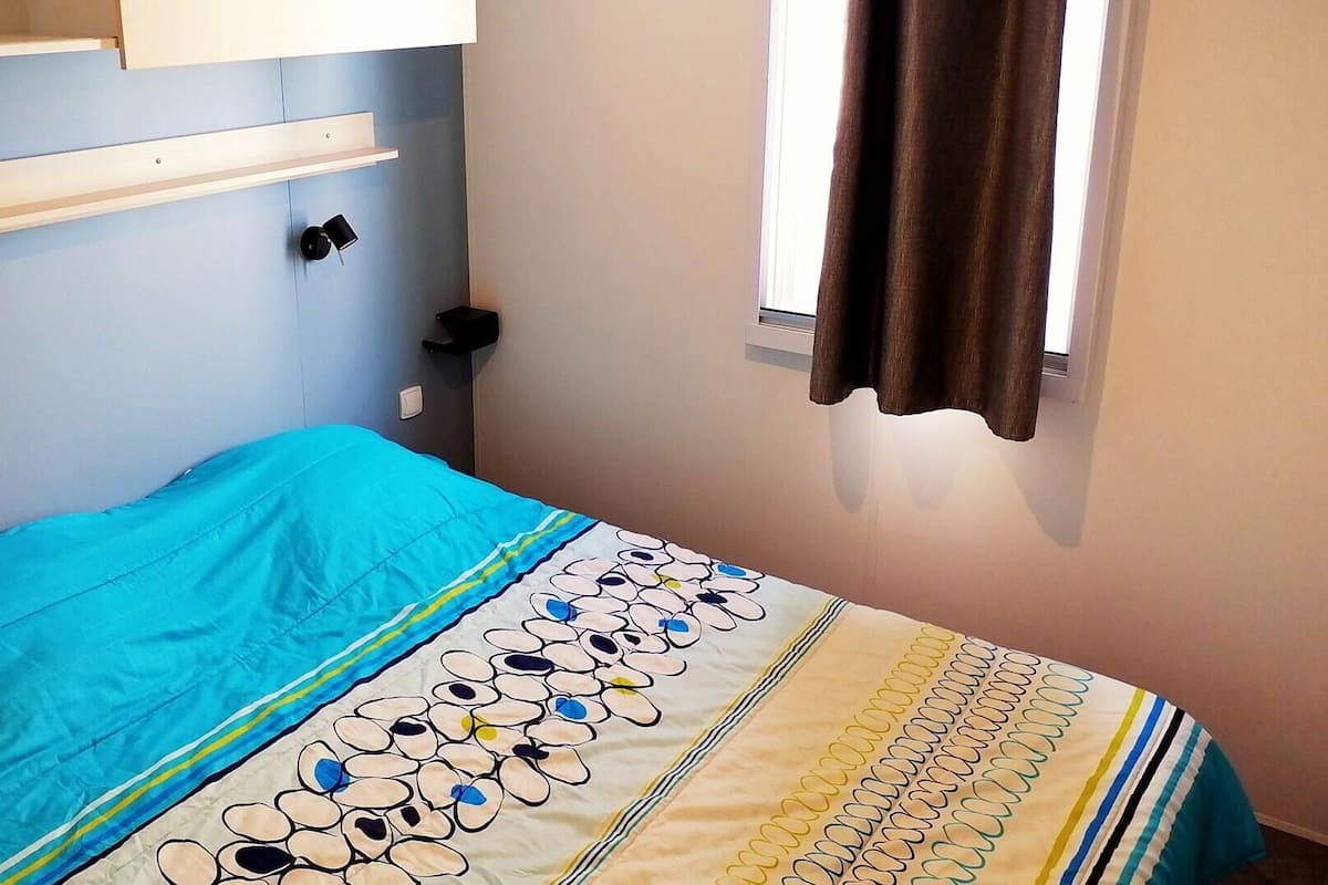 A bedroom with a bed, a window with curtains, and a wall-mounted shelf.