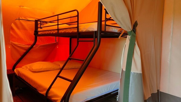 Una cama litera con colchón y almohadas, una escalera metálica y una cortina.