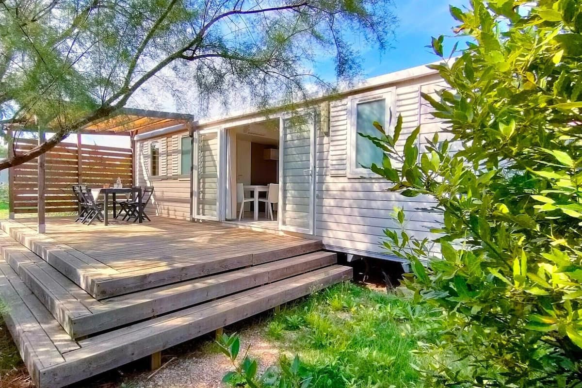 A mobile home with a wooden deck, outdoor seating, and a covered patio area.