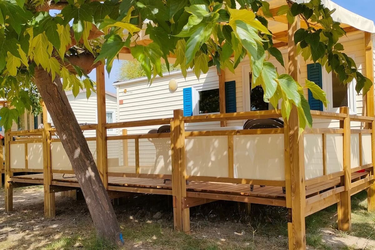 A wooden deck attached to a mobile home with a tree in the foreground.
