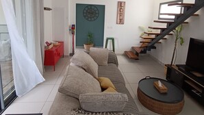 Un salon moderne avec un canapé, une table basse, un téléviseur et un escalier.