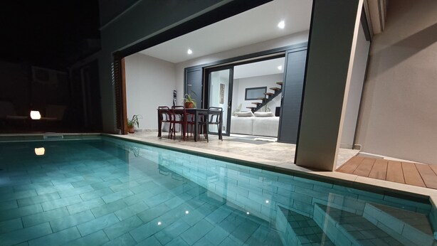 Une piscine intérieure avec un sol carrelé, un coin repas avec des chaises et une table, et un escalier menant à un niveau supérieur.