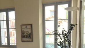 Una habitación con una cama, una mesa con un florero y una planta, y un cuadro en la pared.