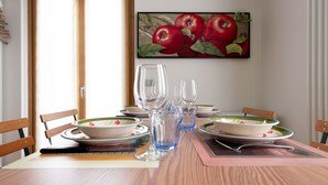 A dining table set with plates, bowls, and glasses, with a painting of apples on the wall behind. - Italianway - Osteglio 15/F - Viola (Valdisotto)