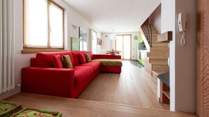 A modern living room with a red sofa, wooden flooring, and a staircase leading to an upper level. - Italianway - Osteglio 15/F - Viola (Valdisotto)