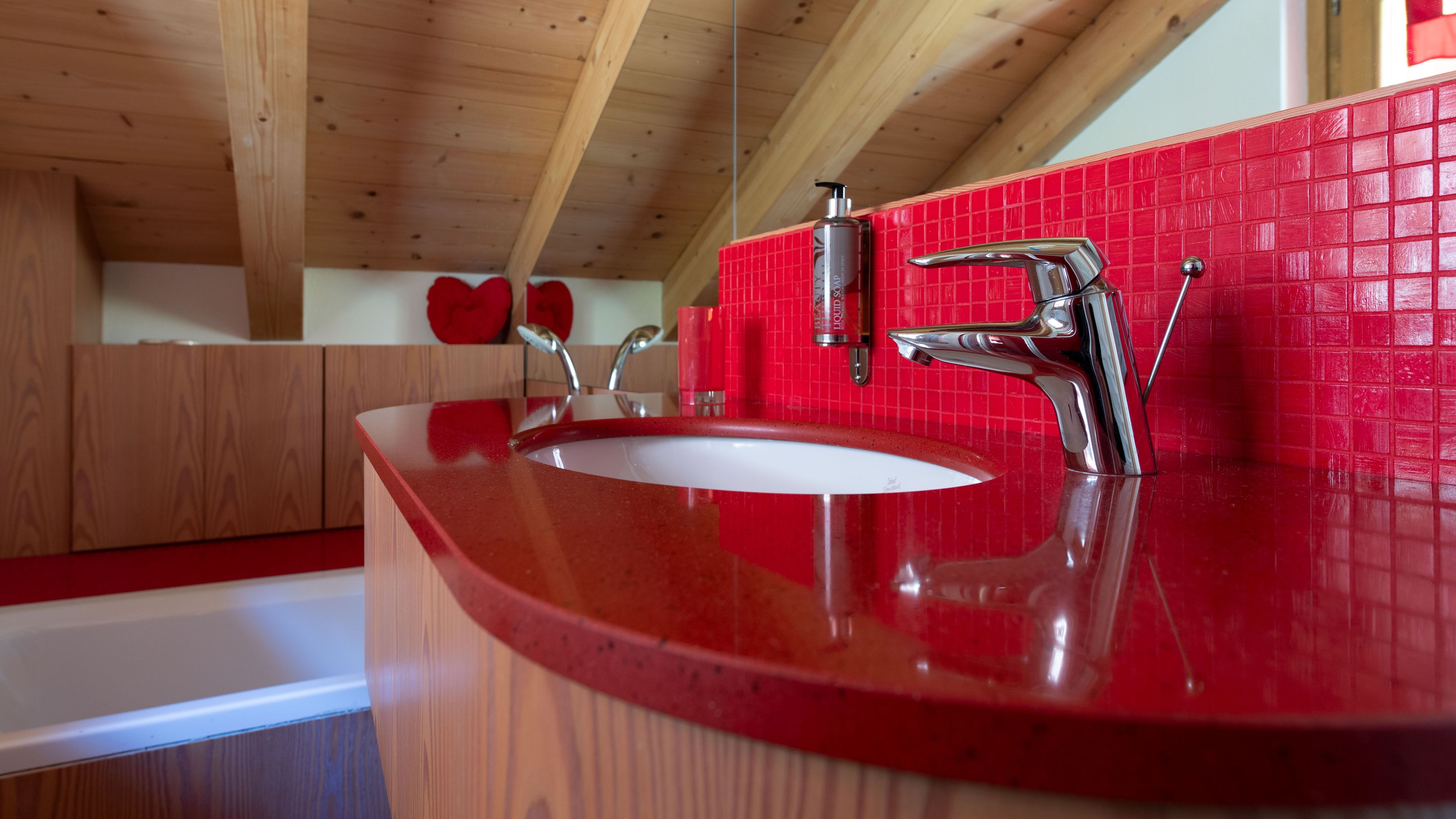 Een badkamer met een rode wasbak, een chromen kraan en een rode betegelde muur.