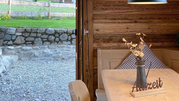A wooden interior with a dining area, a stone wall, and a view of a rural landscape. - Neu Renovierte Ferienwohnung für Bergverliebte (Reichenbach Oberstdorf)