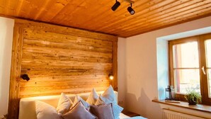 A bedroom with a wooden ceiling, a bed with white bedding, and a window with a view. - Neu Renovierte Ferienwohnung für Bergverliebte (Reichenbach Oberstdorf)