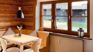 A cozy cabin interior with a wooden ceiling, a dining table with chairs, a window with a view of the outside, and a radiator below the window. - Neu Renovierte Ferienwohnung für Bergverliebte (Reichenbach Oberstdorf)