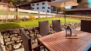 An outdoor patio with a wooden table and wicker chairs, overlooking a mountainous landscape with a building in the background. - Neu Renovierte Ferienwohnung für Bergverliebte (Reichenbach Oberstdorf)