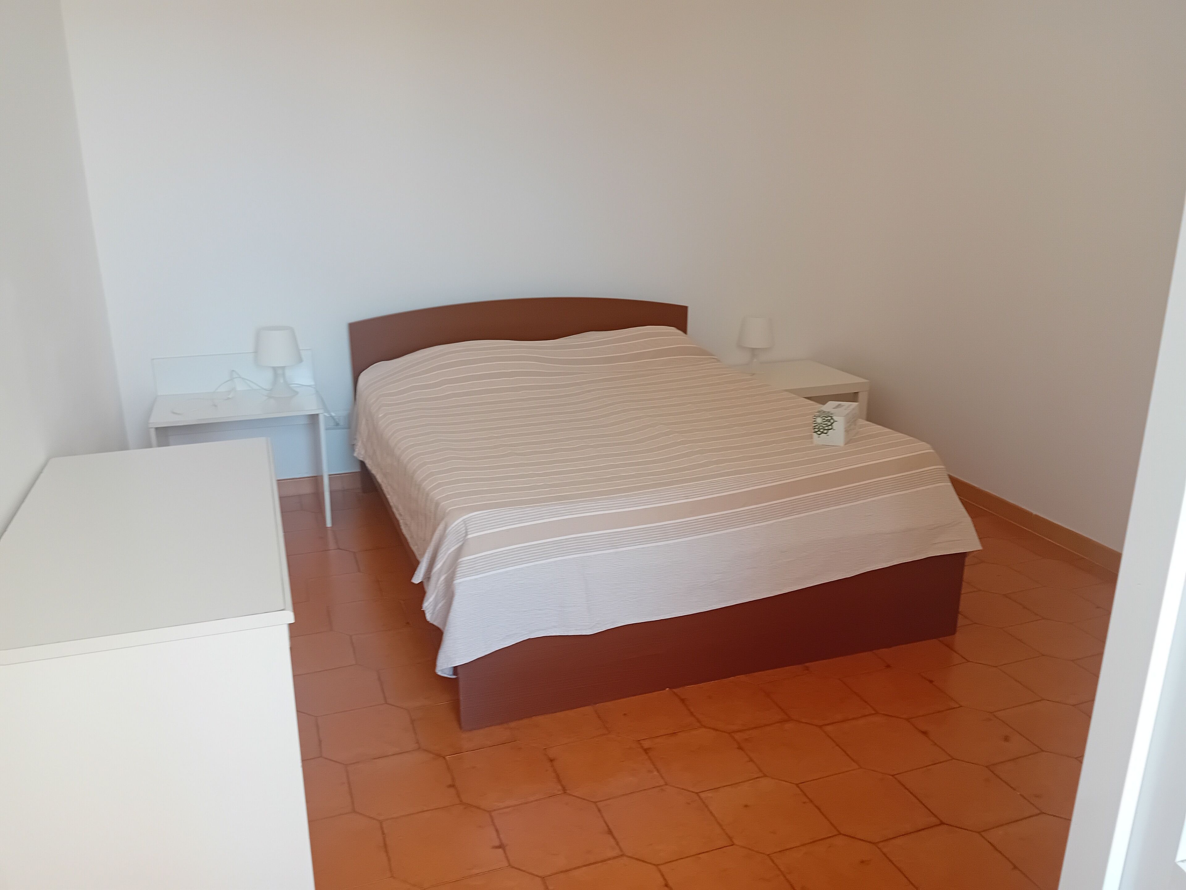 A small, clean room with a single bed, a nightstand, and a bedside table.