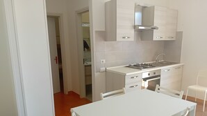 Ett modernt kök med vita skåp, en gasspis och ett diskho. Det finns ett matbord med stolar.