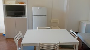 Ett kompakt kök med ett vitt kylskåp, en inbyggd mikrovågsugn och en tv som står på en hylla i ett skåp.