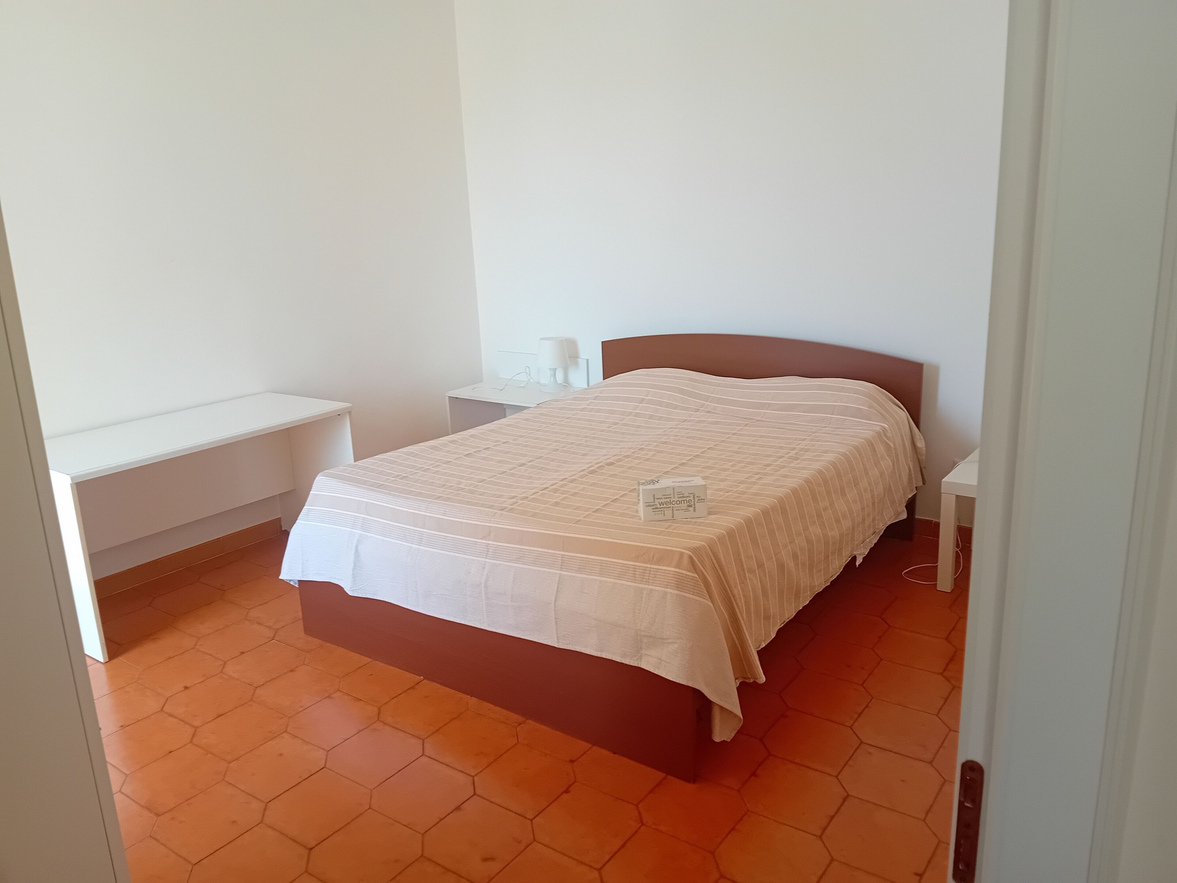 Une chambre à coucher avec un lit, une table de chevet et une commode, le tout adossé à un mur blanc.