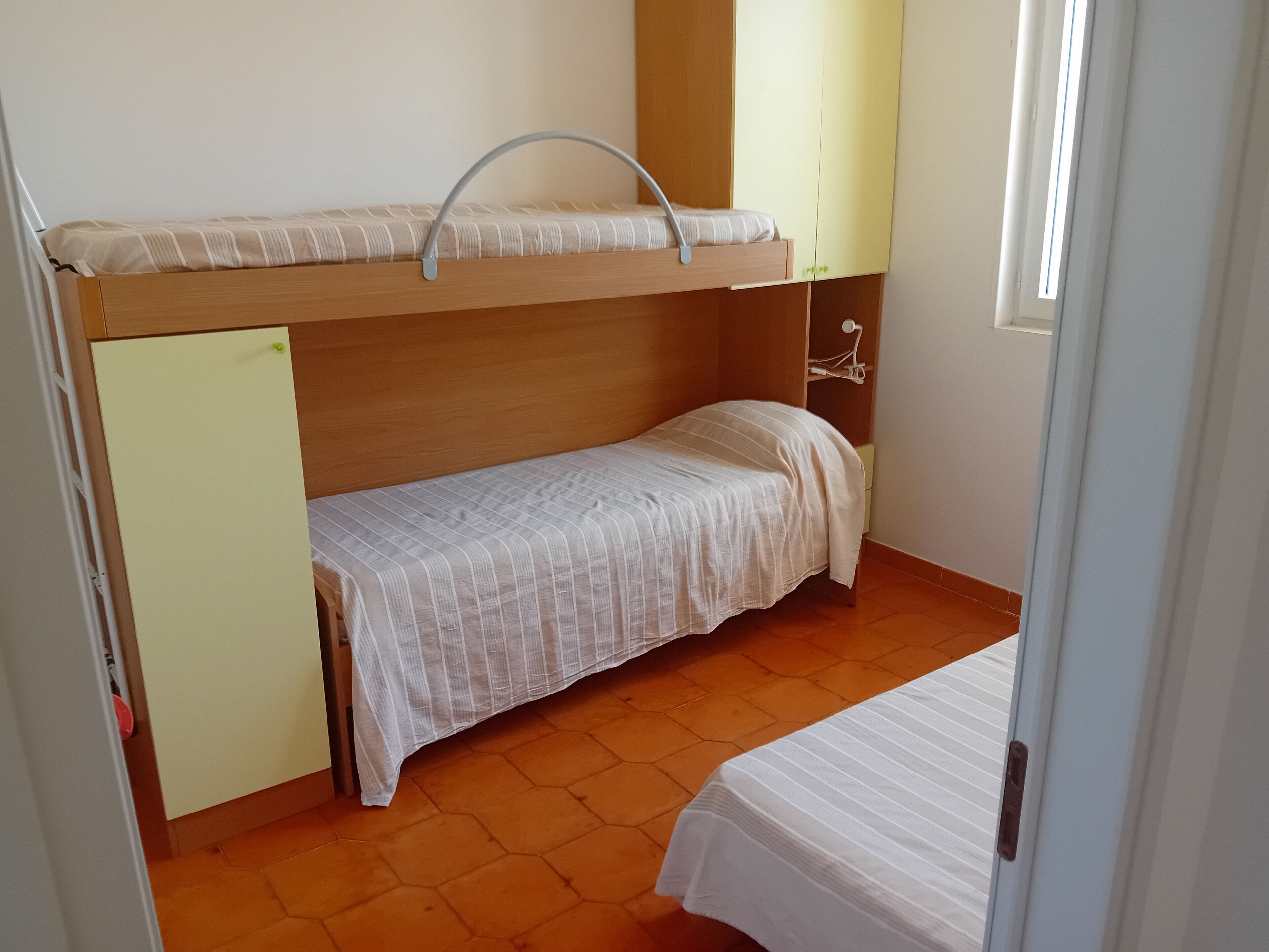 Ein Schlafraum mit Etagenbett, einem hölzernen Kopfteil, einem Einzelbett und einem kleinen Schreibtisch mit Lampe.