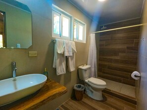 Un baño con tocador de madera, lavamanos blanco, inodoro y zona de ducha.