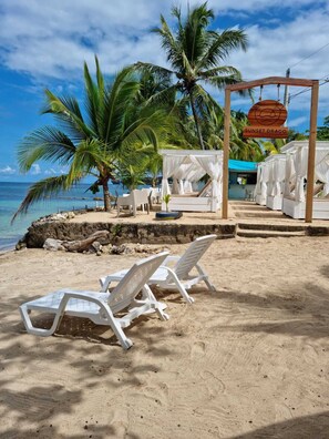 Une cérémonie de mariage organisée sur la plage, avec un auvent, des chaises blanches et des palmiers.