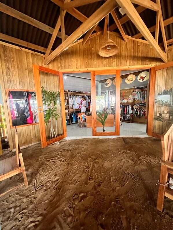 Un intérieur rustique en bois, avec un plafond haut, une grande ouverture centrale donnant sur un magasin de vêtements et un tapis à motifs.