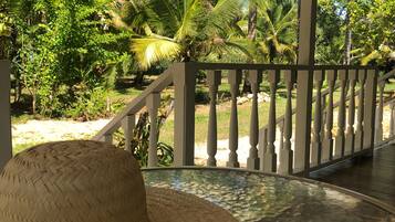 A covered outdoor area with a white railing, a woven hat on the floor, and lush greenery in the background.