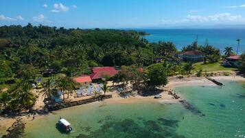 An aerial view of a tropical beach resort with clear waters, palm trees, and a small boat docked near the shore.